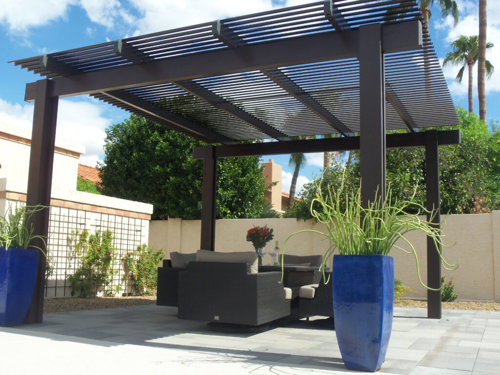 Modern freestanding aluminum louvered pergola with dark frame, outdoor wicker seating set, and tall blue planters