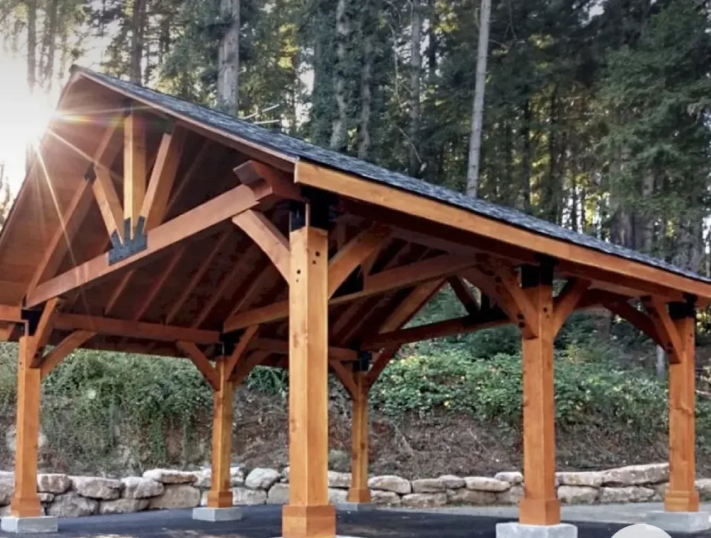 Wooden timber frame pavilion with pitched roof in a forest setting, ideal for outdoor living and gatherings