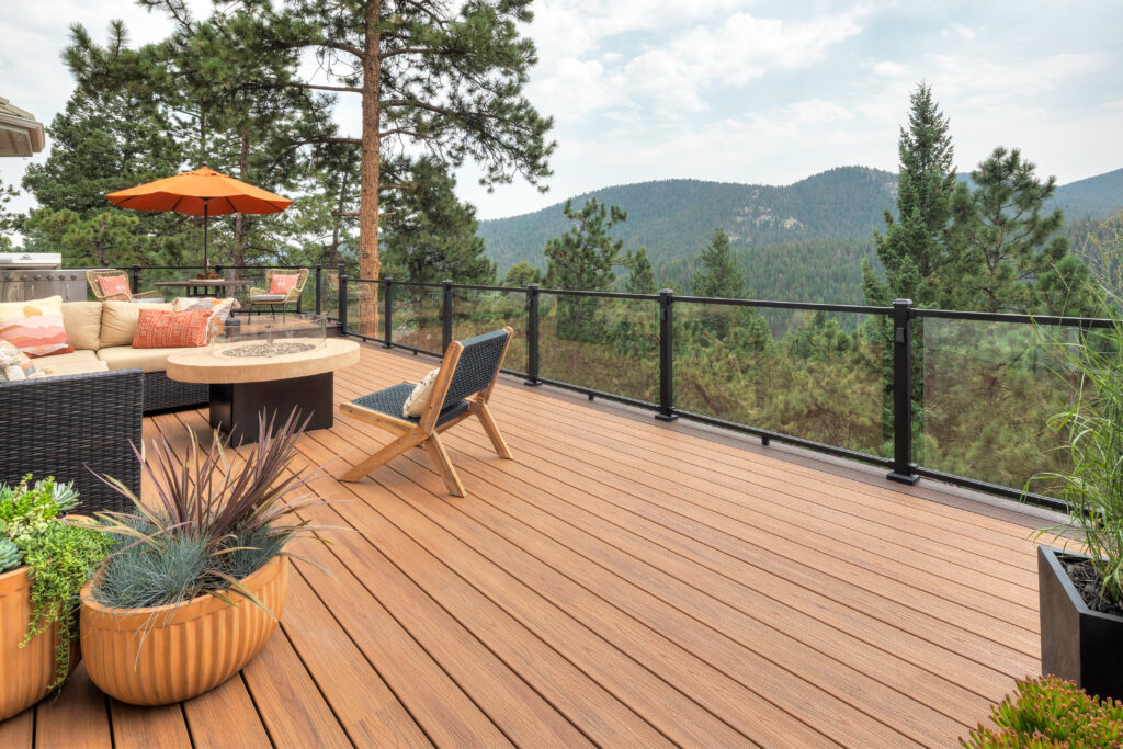 Spacious mountain-view deck with glass railing, outdoor seating, fire pit table, and potted plants