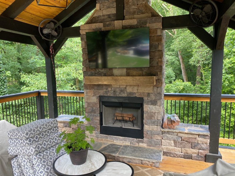 Stone fireplace with a mounted television beneath a timber pavilion